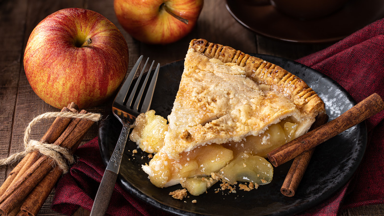 Slice of pie with cinnamon sticks and whole apples
