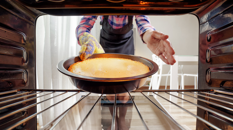 Person removing cheesecake from oven