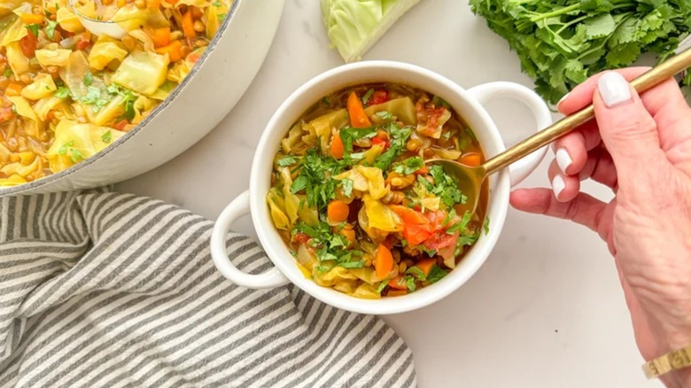 Top view of cabbage and lentil curry soup in a bowl with a hand holding a spoon