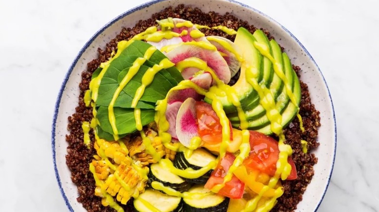 California avocado grain bowl with colorful veggies and a sauce, plated on a table.