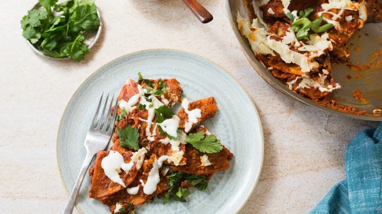 Plated chilaquiles gojos garnished with fresh green herbs with a pan and more fresh herbs on the side