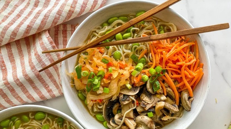 Top view of a kimchi ramen bowl with mushrooms, kimchi, carrots, noodles, and scallions
