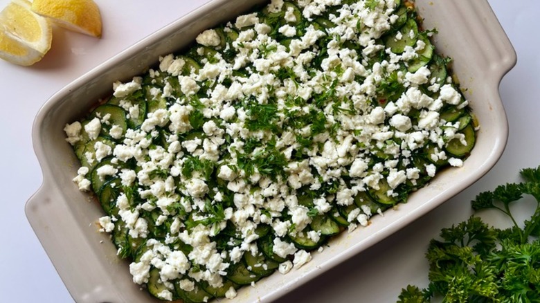 View from above of zucchini casserole in a dish on a table with lemon and parsley garnish