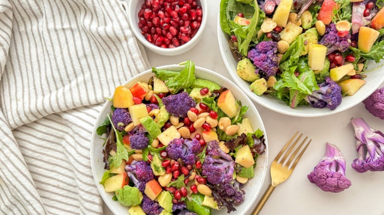 Top view of oven-roasted purple cauliflower salad in two bowls with pomegranate