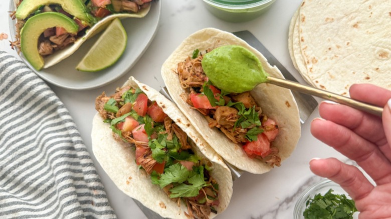Plant-based jackfruit carnitas tacos plated with guacamole being put on top