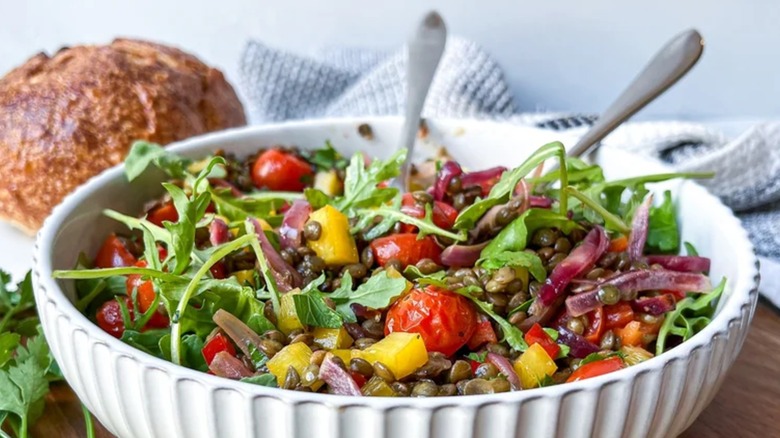Plated roasted garlic tomato lentil bowl with colorful veggies and herbs on a table