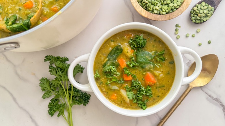 Top view of a vegan split pea soup in a bowl with a spoon, split peas, and fresh parsley on a table