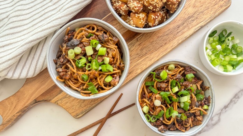 Vegetarian mushroom-walnut dan dan noodles in bowls with chop sticks and green onion garnish