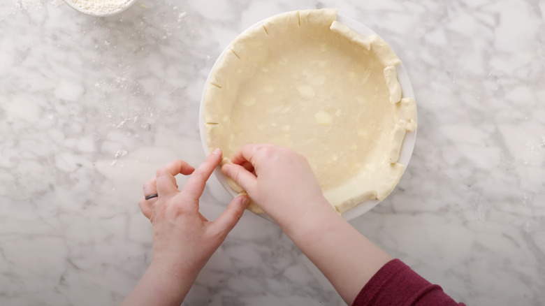 hands making a checkerboard pie crust on granite counter with hands