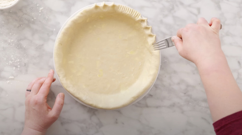 Person crimping pie crust with fork and scalloped edges