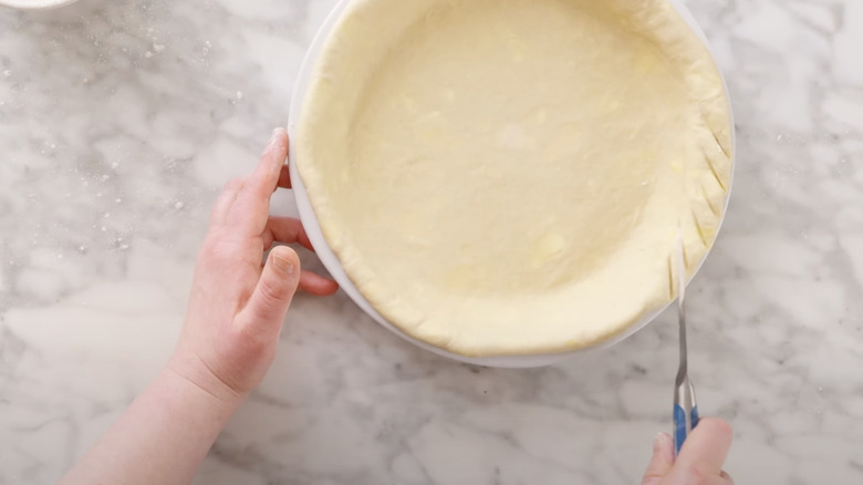 hands using a knife to make slits in pie crust