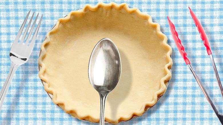 unbaked pie shell in tin surrounded by kitchen utensils