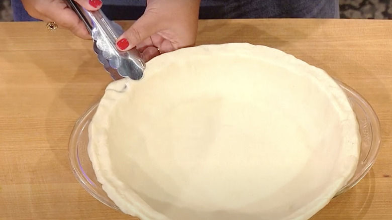 Person pressing pie crust with kitchen tongs