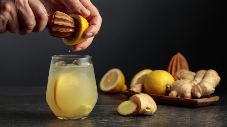 hands using wooden citrus juicer with lemons, ginger, and beverage