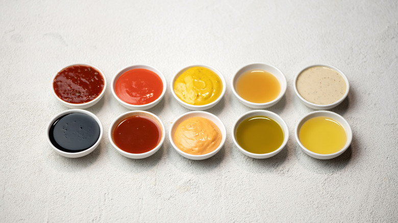 Big Set of colored sauces in Crockery. Different sauces, mayonnaise, mustard, soy sauce, oil and ketchup on white background. Top side view. Tasty food. Kitchen utensils.