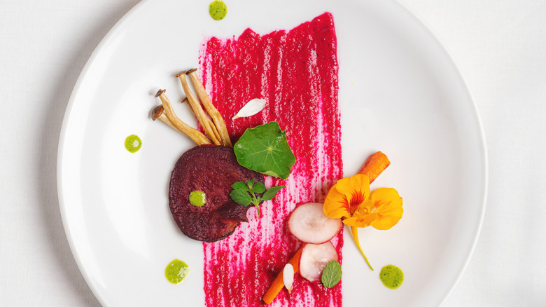 Elegant gourmet fine dine carrot, radish, mushroom with a brushed beetroot reduction and garnished with nasturtium flower and petals.