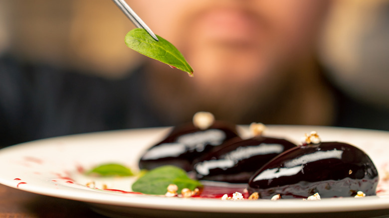 close-up in a professional kitchen the chef in black gloves decorates the dessert with tweezers