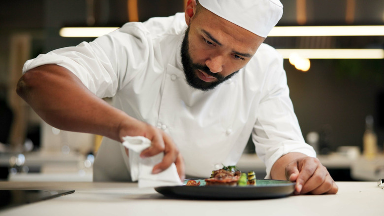 Man, chef and serious with plate in kitchen at restaurant for fine dining, meal and creativity. Male employee, professional and cooker with food for culinary, hospitality and catering service