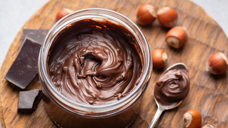 container of hazelnut spread on wooden board with hazelnuts