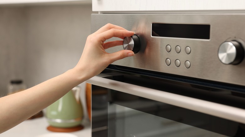 Hand turning the knob on an oven