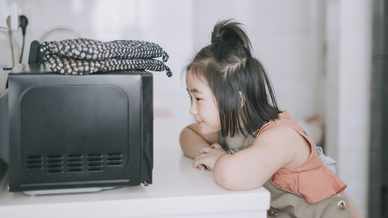 Little girl looking at microwave