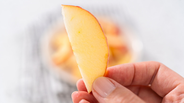 Person holding an apple slice with fingers