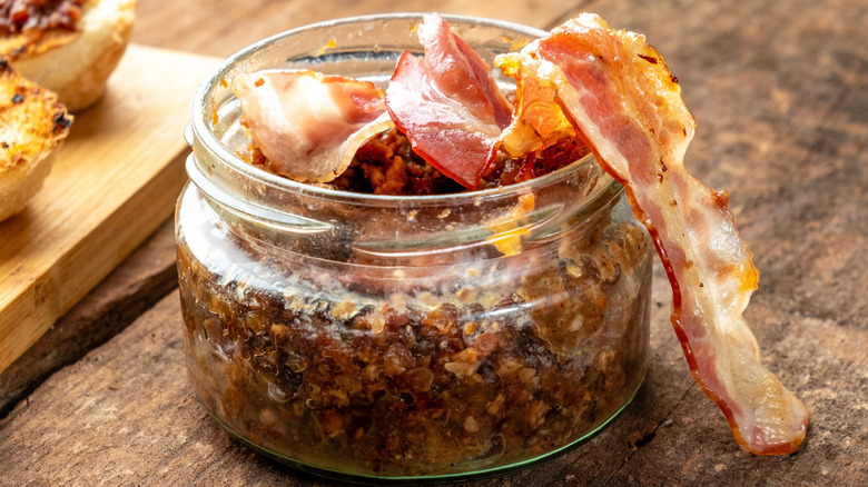 Bacon jam in glass jar with a cooked bacon slice