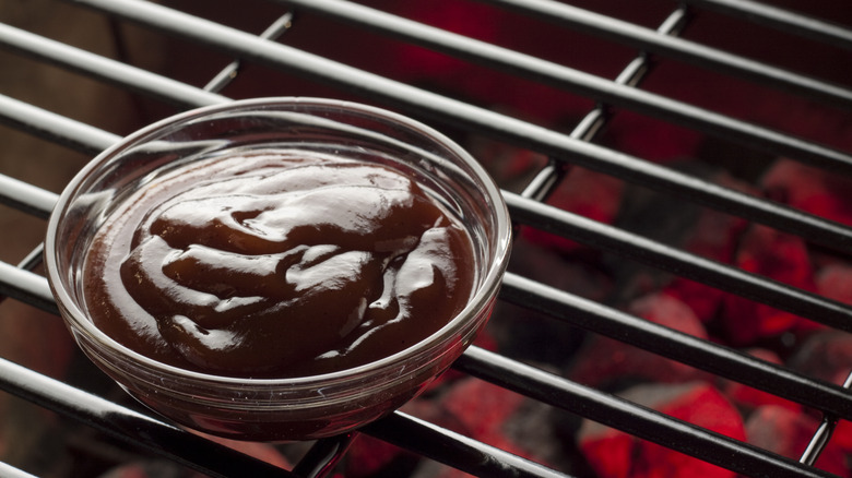 Container of barbecue sauce on grill