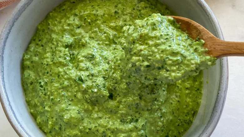 A spoon holding some fresh pesto from a bowl