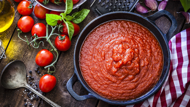 a pot of smooth marinara sauce on table with vine tomatoes