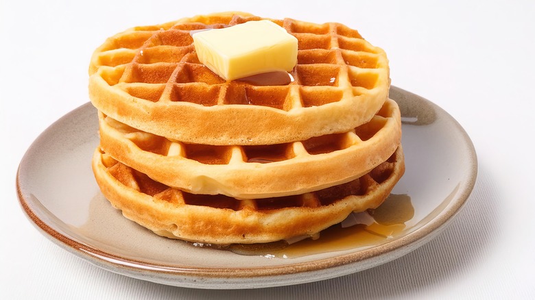 stack of Belgian waffles with crispy crust topped with butter and syrup on plate