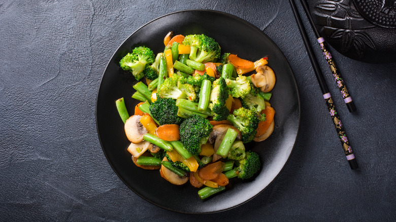 stir fried vegetables on black plate with chopsticks on the side