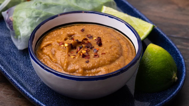 satay peanut sauce in a bowl next to summer rolls and limes