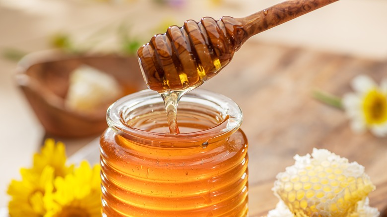 organic honey in glass jar with flowers in the background