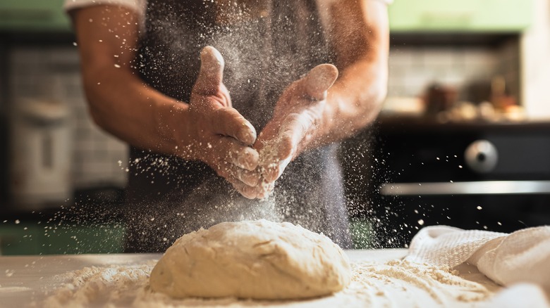 A man spraying flour over dough