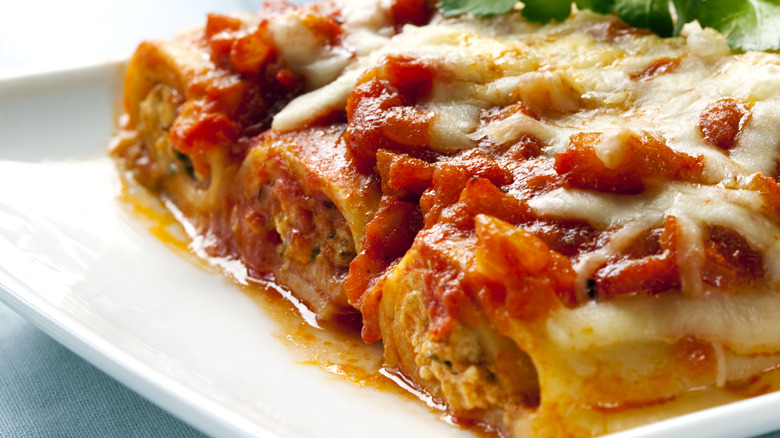 Three cannelloni topped with melted cheese and tomato