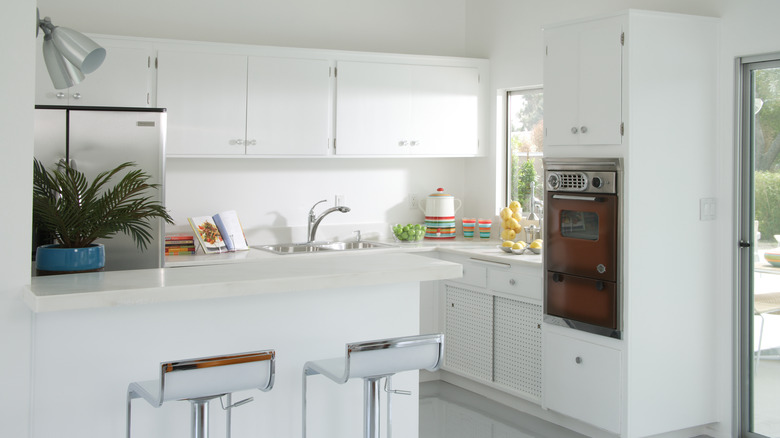 Shot of all-white kitchen with a kitchen island, countertops, sink, bar stools, and cabinets