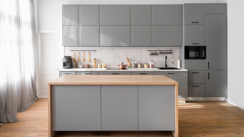 Kitchen with grey island and cabinets, wooden counter, wooden floor and a marble backsplash