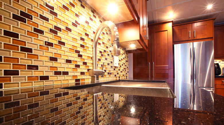 Kitchen counter and sink with mosaic tile backsplash and wooden kitchen cabinets in the back