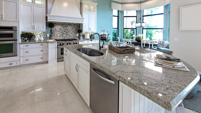 Wide shot of all-white kitchen with stainless steel appliances and granite countertops