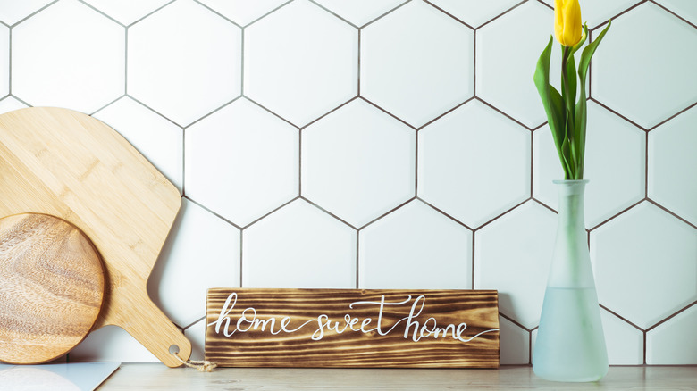 Wooden home sweet home sign oh kitchen counter between a cutting board and a yellow tulip flower