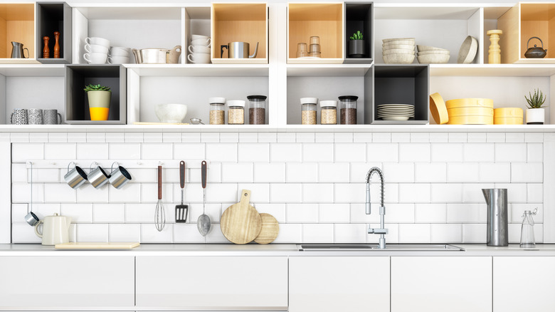 All-white kitchen with open shelving stuffed with various kitchen items above subway tile backsplash