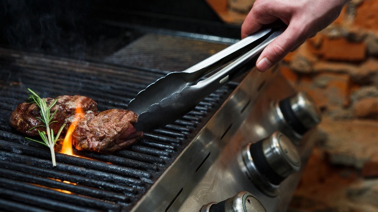 Hand turning steak on grill