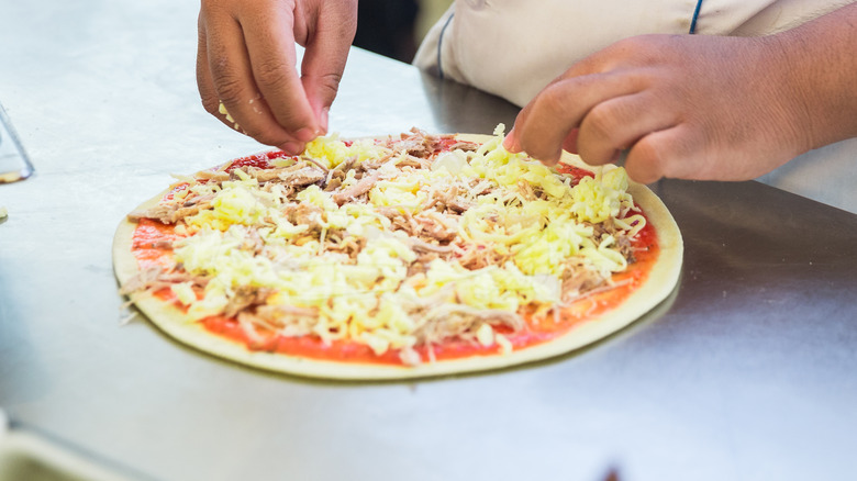 Person topping pizza with pineapple