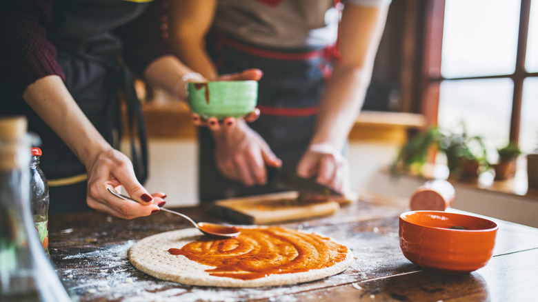 People spreading sauce on pizza