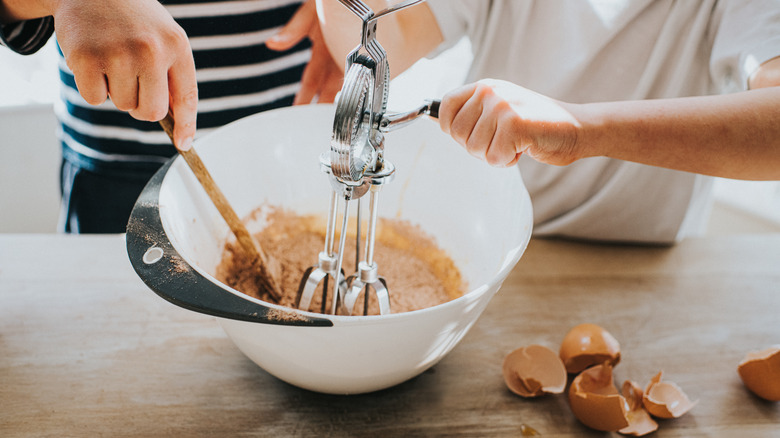 People using hand-beater in mixing bowl in the kitchen