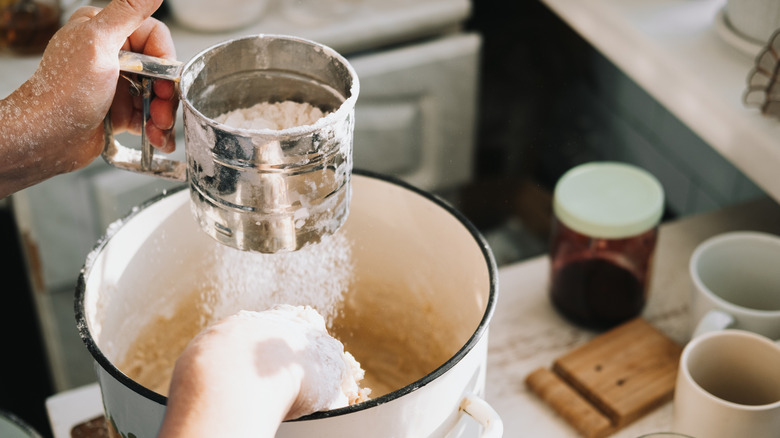 Person sifting flour into large bowl