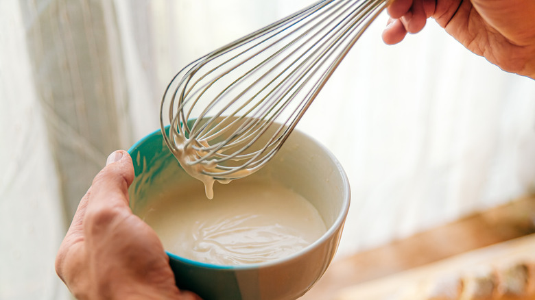 Person holding whisk dripping cake batter and bowl of mixture