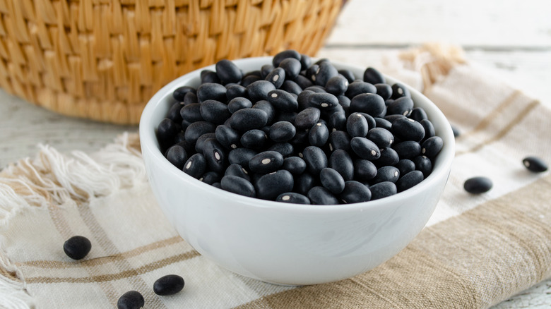 Dry black beans in white bowl sitting on cloth napkin