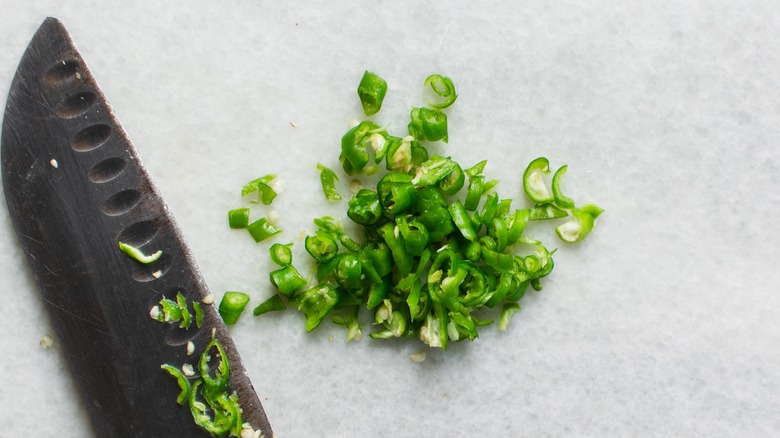 Diced green chilies on white background next to chef's knife